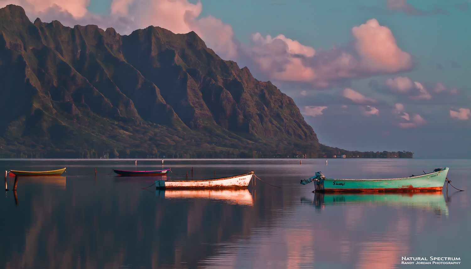 The sunrise light creates a new day as it washes over fishing boats and the Ko'olau Mountains, Kaneohe Bay, Ohau, Hawaii.